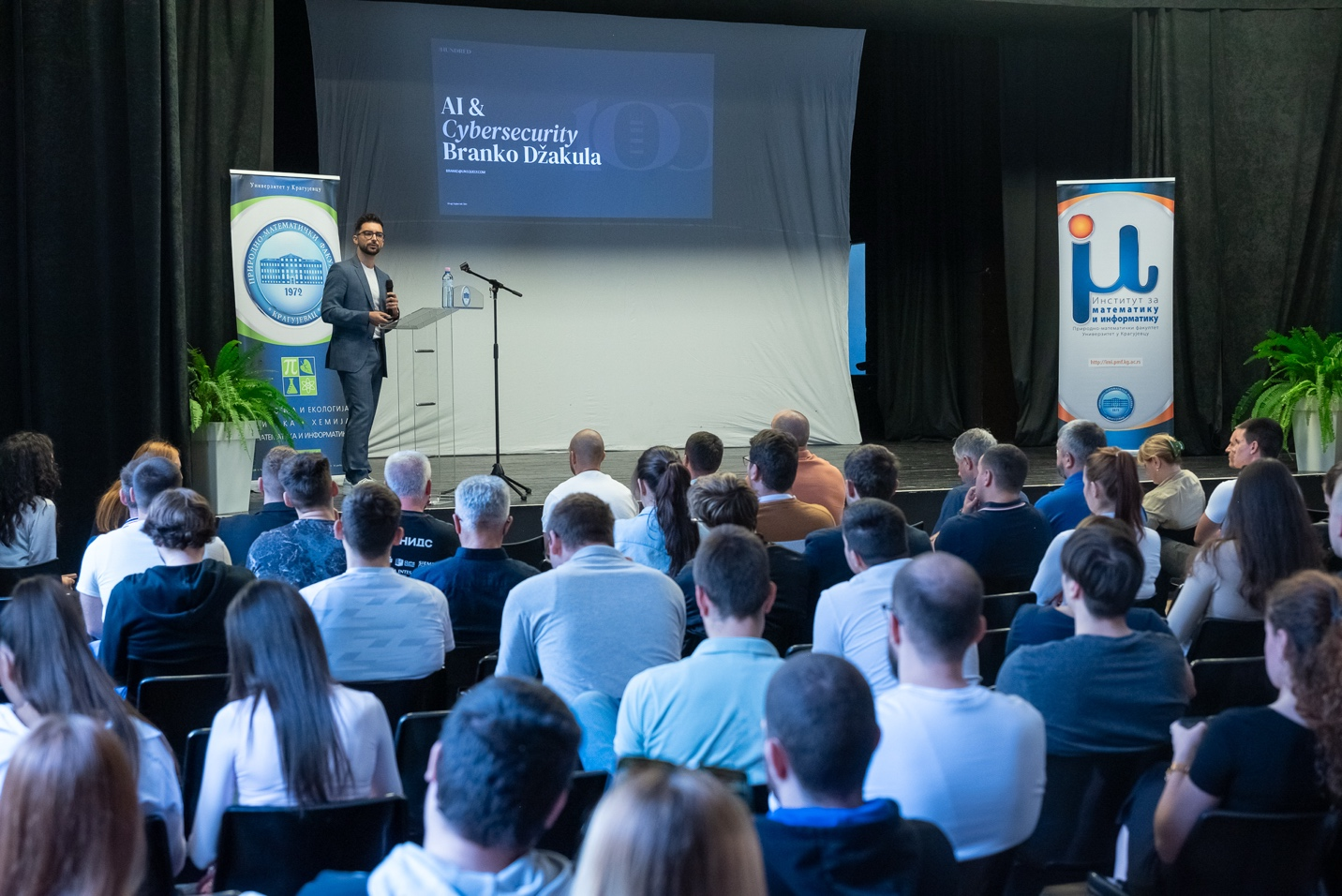 Branko Džakula on stage at the University of Kragujevac presenting on AI and cybersecurity to a full audience.